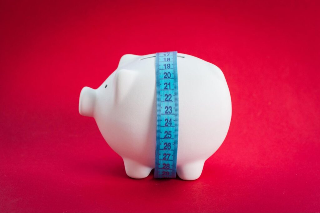 A piggy bank wrapped in measuring tape signaling financial inefficiency